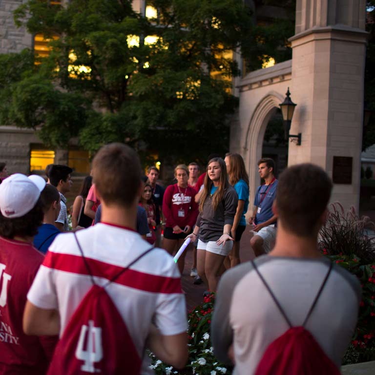 a young woman talks to a group in front of the sample gates